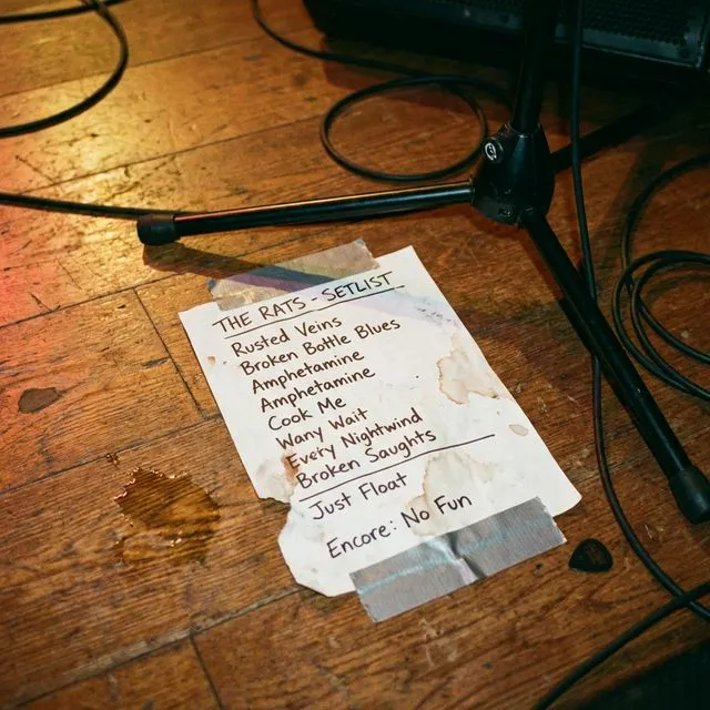 A handwritten setlist taped to a stage floor next to a microphone stand